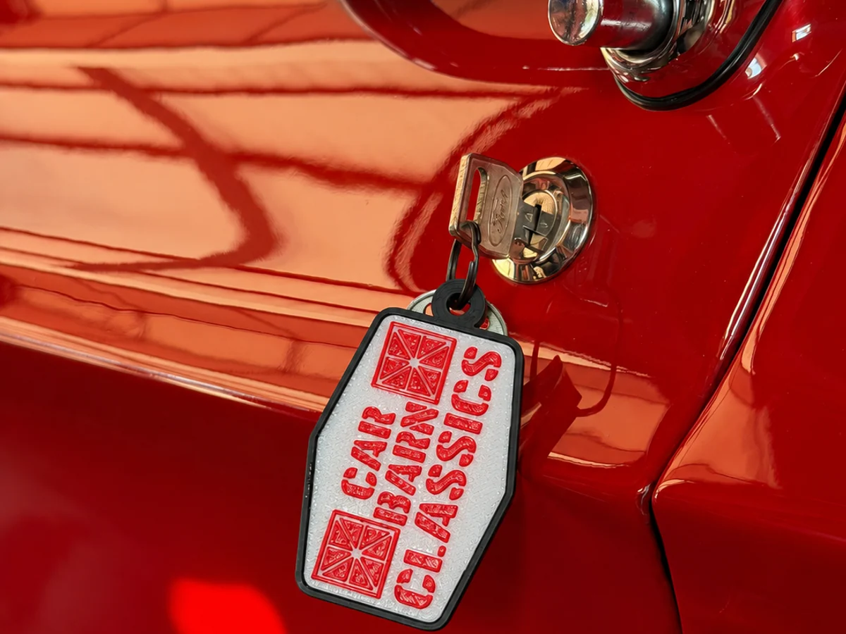 Custom red, white, and black 3D printed logo keychain attached to a classic car key